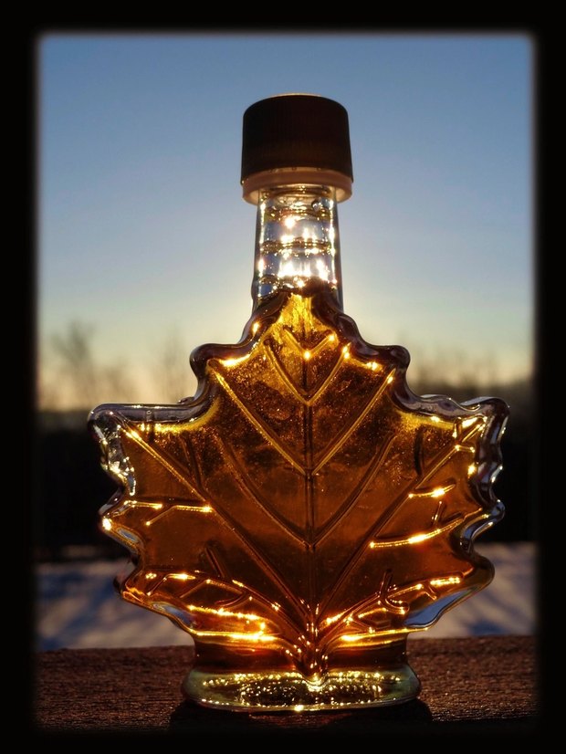 A maple-leaf-shaped bottle of syrup glowing amber against a dusk sky